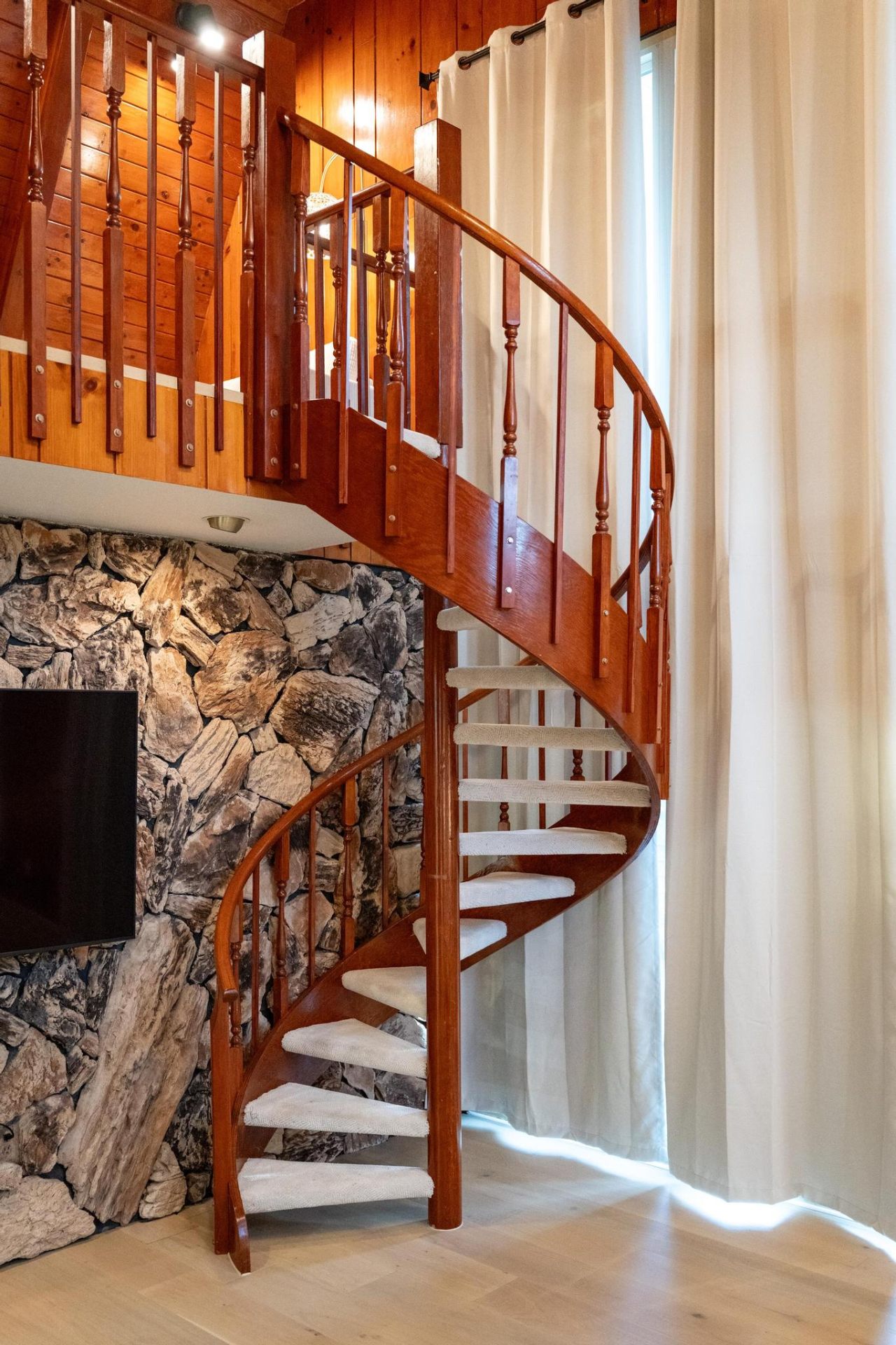 Cherry-wood spiral staircase against natural stone wall